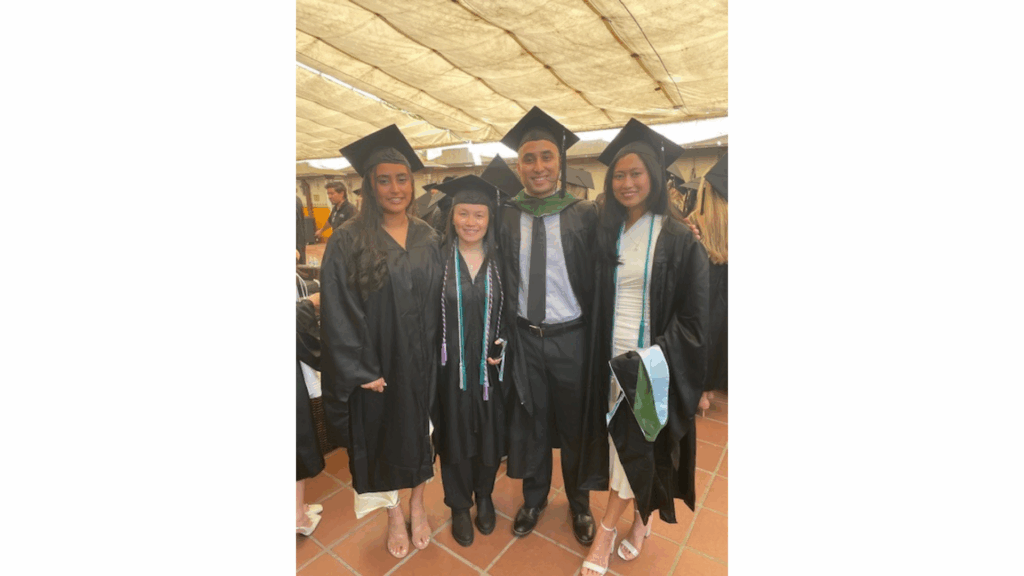 Four people in black graduation regalia at a graduation ceremony.