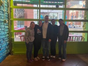 Five people standing in front of a window posing for a picture.